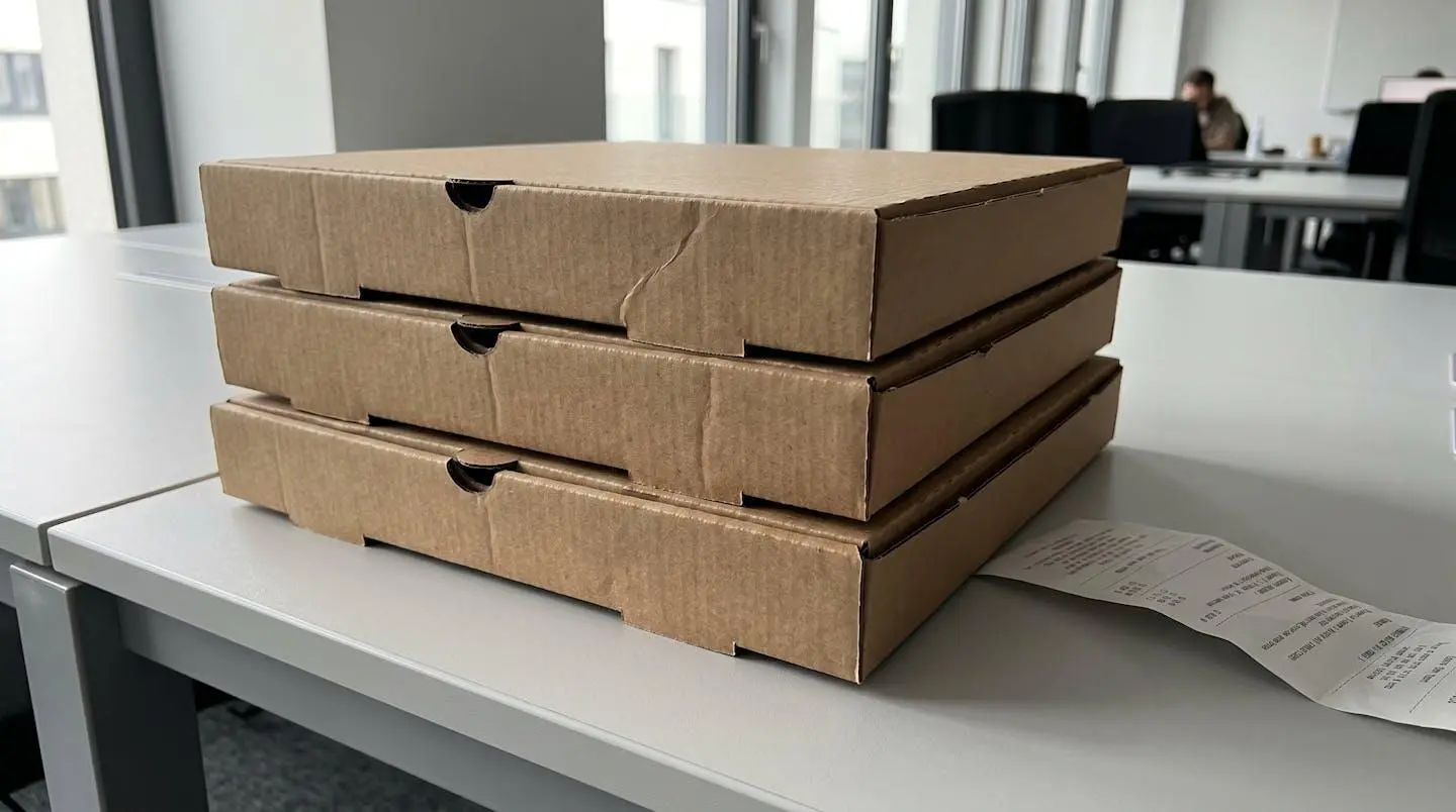 Pile de cartons de pizzas livrés avec un bordereau de commande sur un comptoir de bureau